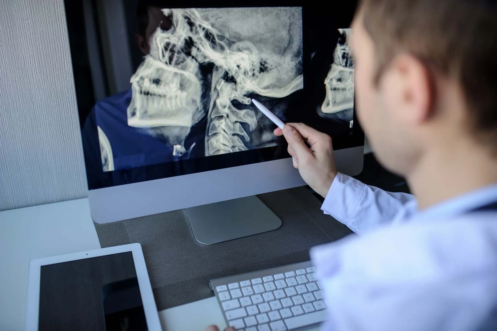 Doctor pointing at a cervical spine X-ray on a computer screen with a pen.
